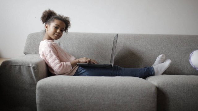 A little girl on a sofa with a laptop on her lap